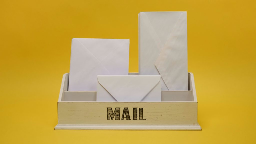 White envelopes neatly arranged in a mail organizer against a vibrant yellow background.